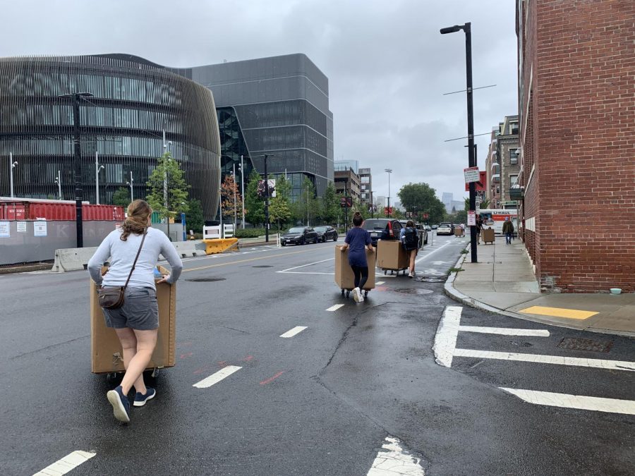 A student and her family wheel bins down Columbus Avenue in the rain. 