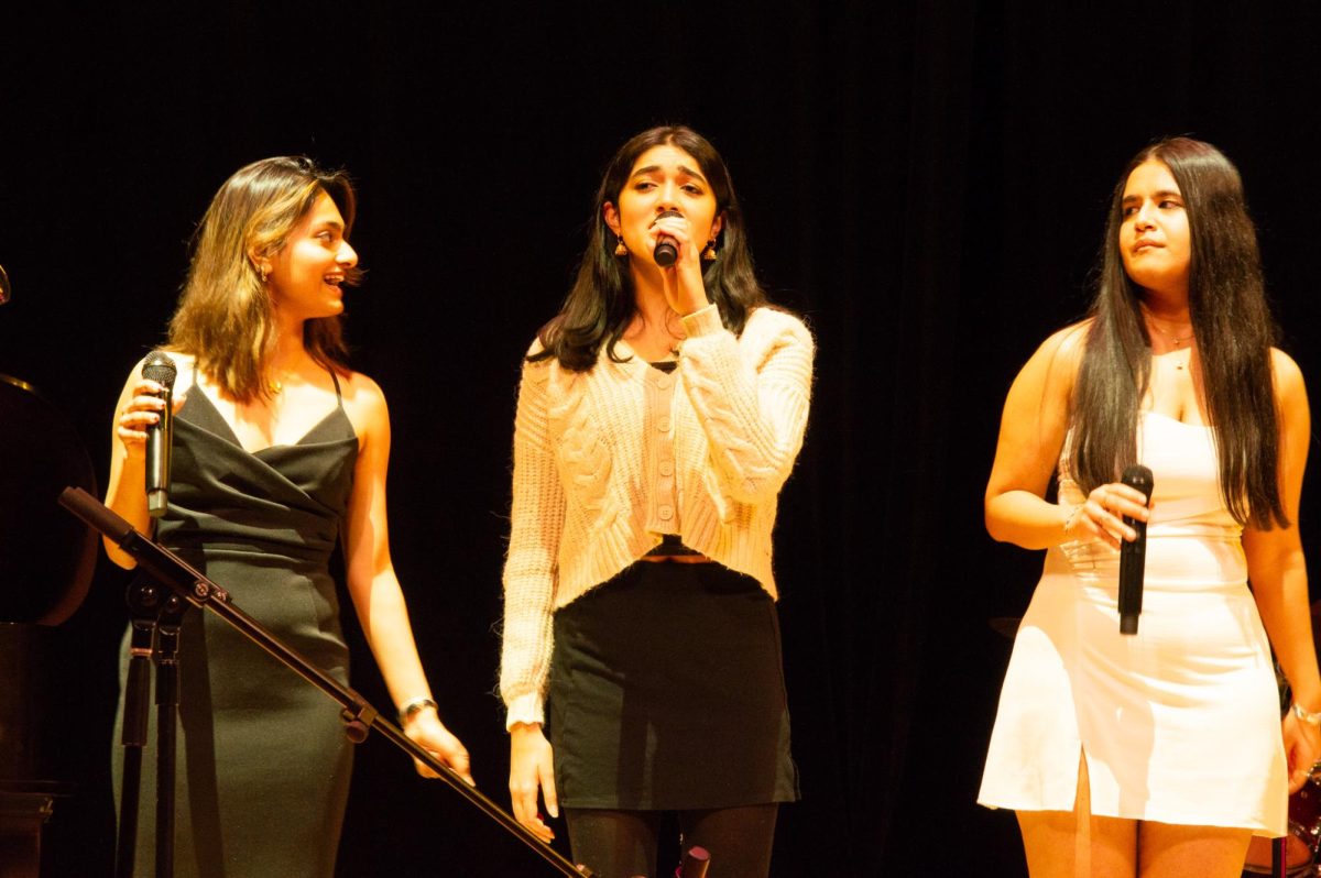 Two singers watch as the center performer sings during a Bollywood set. The performers enjoyed themselves on stage, dancing and interacting with the audience.