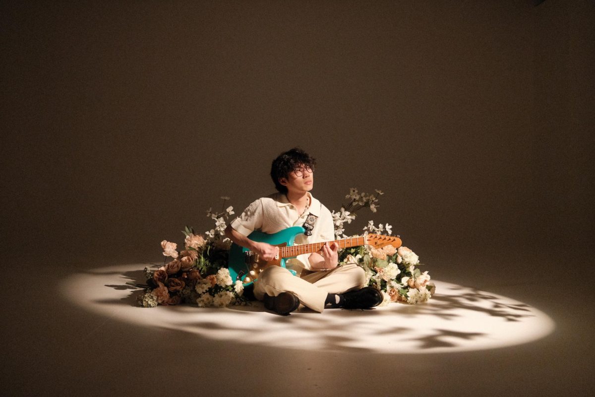 While sitting in a pile of flowers and holding a teal electric guitar, hongjoin poses for a photo. Cheng, or hongjoin, opened for Grent Perez during the Asian American Heritage Month showcase Jan. 26. Photo courtesy hongjoin.
