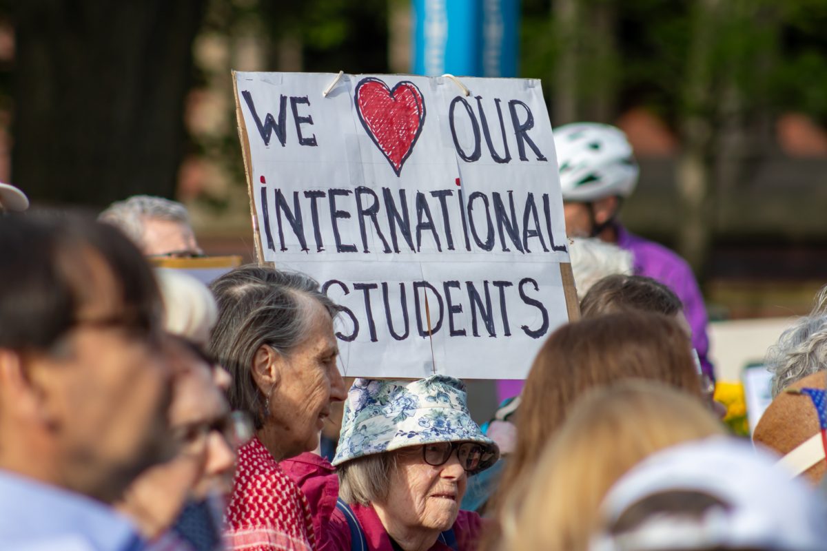 A demonstrator hoists a sign above their head that reads, "We [heart] our international students." Among the posters were some listing international scientists, while other protesters held American flags.